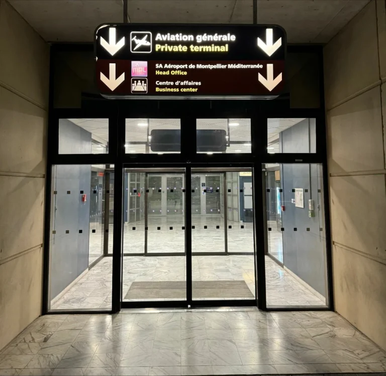 Entrée vitrée de l'aviation générale et du terminal privé de l'aéroport de Montpellier Méditerranée avec un panneau directionnel au-dessus.