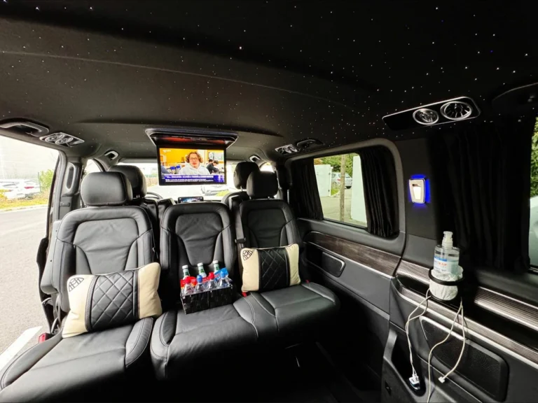 L'intérieur d'un Mercedes V-Class montrant des sièges en cuir avec un ciel étoilé à LED au plafond et un écran affichant des nouvelles télévisées.
